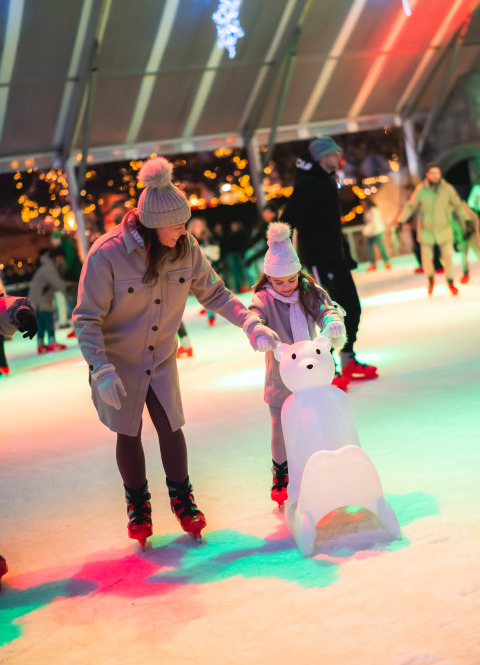Mutter und Tochter beim Eislaufen in der Halle Schaelsbergerbosch mit bunten Lichtern und Eisbärhilfe.