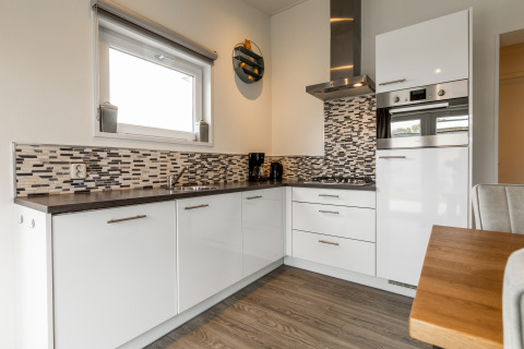 Moderne keuken met witte kasten, mozaïekwand, oven en houten tafel in een gezellige Nederlandse lodge.