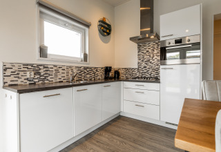 Moderne keuken met witte kasten, mozaïekwand, oven en houten tafel in een gezellige Nederlandse lodge.