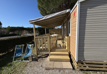 Mobile Home ‘New Horizon’ with covered wooden veranda and lounge chairs at Flower Camping Provence Vallée, France.