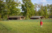 Ein Kind im roten Hemd läuft auf einer Wiese Richtung Wellness Luxe Lodge bei Landrijk de Reesprong, Niederlande.