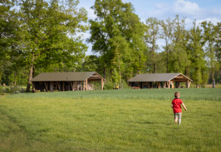Un bambino con maglia rossa corre verso la Wellness Luxe Lodge a Landrijk de Reesprong, Paesi Bassi, su un prato verde.