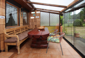 Veranda coperta al Holiday home «Susanne 58 qm» in Germania con panca in legno, tavolo e pareti di vetro.