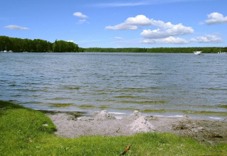 Vista sul lago alla Holiday home «Susanne 58 qm» in Germania, con erba verde, cielo blu e una barca.