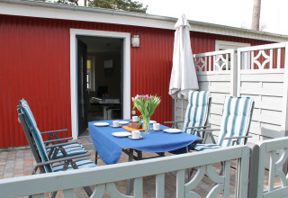Buitenpatio bij lodge 'Am Strand' in Duitsland met tafel, gestreepte stoelen en bloemenvaas.