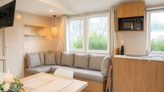 Interno lodge Vakantiehuis Celestia con divano ad angolo, tavolo da pranzo, cucina e ampie finestre.