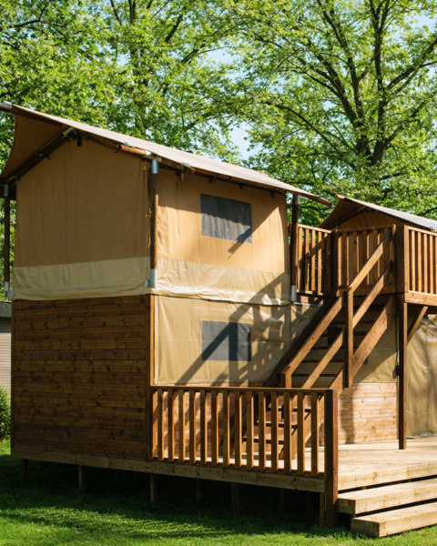 Boomhut-tent op twee verdiepingen met houten trap bij Holiday park Mölke, Nederland, omgeven door bomen.