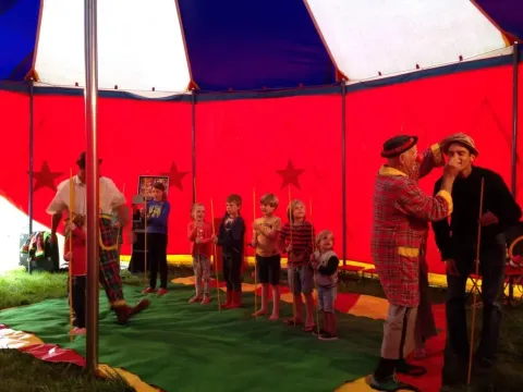 Bambini partecipano a un laboratorio circense con clown sotto un colorato tendone al campeggio Les Trexons, Francia.