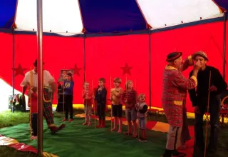 Bambini partecipano a un laboratorio circense con clown sotto un colorato tendone al campeggio Les Trexons, Francia.