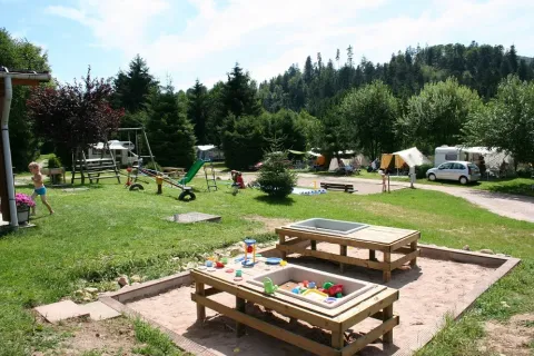 Area giochi e campeggio con tende e bambini al campeggio Les Trexons, Grand Est, Francia in una giornata di sole.