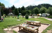Playground and camping area with tents and children at Campsite Les Trexons in Grand Est, France on a sunny day.
