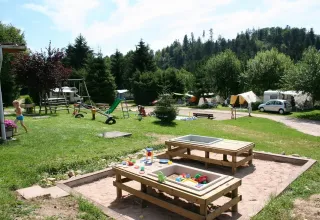 Area giochi e campeggio con tende e bambini al campeggio Les Trexons, Grand Est, Francia in una giornata di sole.