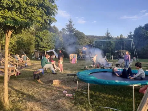 Famiglie si riuniscono attorno al fuoco e si divertono sul trampolino al campeggio Les Trexons, Grand Est, Francia.