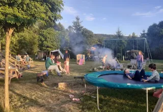 Famiglie si riuniscono attorno al fuoco e si divertono sul trampolino al campeggio Les Trexons, Grand Est, Francia.