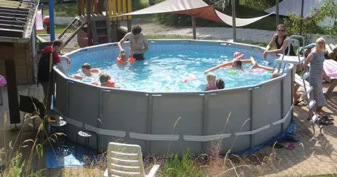 Bambini e adulti si divertono in una piscina fuori terra circolare al Campeggio Les Trexons, Grand Est, Francia.