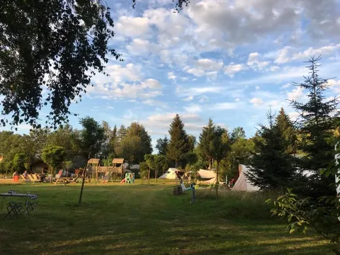 Vista del campeggio Les Trexons con tende, area giochi e alberi sotto un cielo azzurro a Grand Est, Francia.