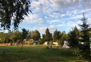 Vista del campeggio Les Trexons con tende, area giochi e alberi sotto un cielo azzurro a Grand Est, Francia.