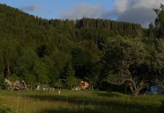 Foto del campeggio Les Trexons a Grand Est, Francia, tra alberi verdi, area giochi e una casetta di legno.