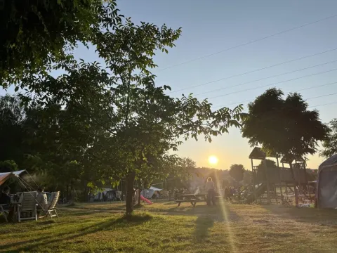 Tramonto al campeggio Les Trexons in Grand Est, Francia, con area giochi, alberi e tende sullo sfondo.