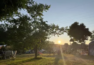 Tramonto al campeggio Les Trexons in Grand Est, Francia, con area giochi, alberi e tende sullo sfondo.