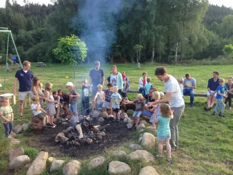 Bambini e adulti si godono un falò al Campeggio Les Trexons nel Grand Est, Francia, immersi nella natura.