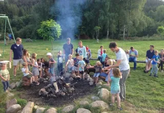 Bambini e adulti si godono un falò al Campeggio Les Trexons nel Grand Est, Francia, immersi nella natura.