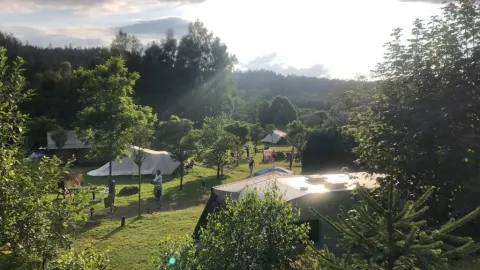 Vista del campeggio Les Trexons a Grand Est, Francia, con tende, alberi e ospiti in una giornata soleggiata.