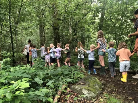 Bambini e adulti formano una fila esplorando il bosco verde al Campeggio Les Trexons, in Francia.