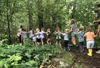 Bambini e adulti formano una fila esplorando il bosco verde al Campeggio Les Trexons, in Francia.