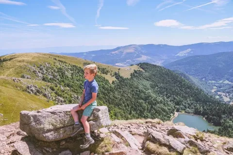 Ragazzo seduto su una roccia con vista sulle montagne al Campeggio Les Trexons, Grand Est, Francia.