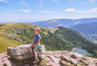 Ragazzo seduto su una roccia con vista sulle montagne al Campeggio Les Trexons, Grand Est, Francia.