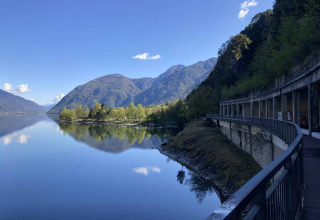 Vista sul lago tranquillo al Campeggio Belvedere in Lombardia, Italia, con montagne e alberi sotto il cielo sereno.