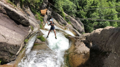 Persona su una zipline sopra rocce e fiume al Campeggio Belvedere, parco vacanze in Lombardia, Italia.