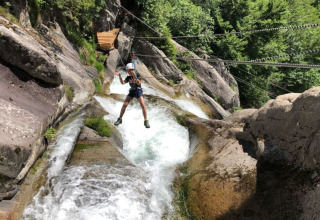 Persona su una zipline sopra rocce e fiume al Campeggio Belvedere, parco vacanze in Lombardia, Italia.