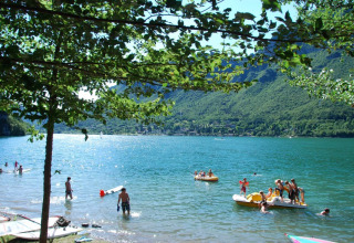 Parc de vacances avec glamping : visiteurs profitant du lac et des montagnes verdoyantes en été.