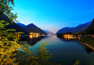 Vista serale su lago e montagne dal campeggio Belvedere in Lombardia, Italia, con luci riflesse sulla riva.