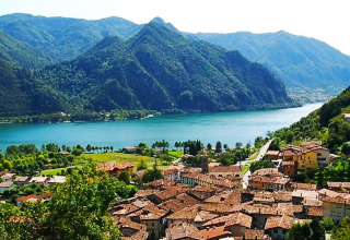Panorama di Idro in Lombardia, Italia, con case dai tetti rossi, lago cristallino e montagne verdi circostanti.