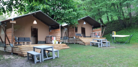 Due tende glamping con terrazze e tavoli da picnic al Campeggio Belvedere, Lombardia, Italia, immerse nel verde.