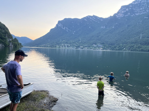 Uomo e bambini al lago con montagne al campeggio Belvedere nel parco vacanze in Lombardia, Italia.