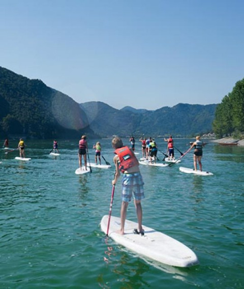 Gruppo di persone fa paddleboarding su un lago vicino a Idro BS, Lombardia, Italia, in una giornata di sole.
