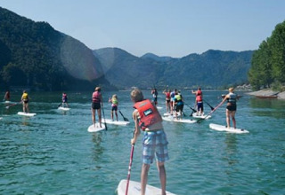 Gruppo di persone fa paddleboarding su un lago vicino a Idro BS, Lombardia, Italia, in una giornata di sole.