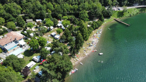 Vista aerea del Campeggio Belvedere in Lombardia, Italia, con lago, tende, caravan e alberi verdi.