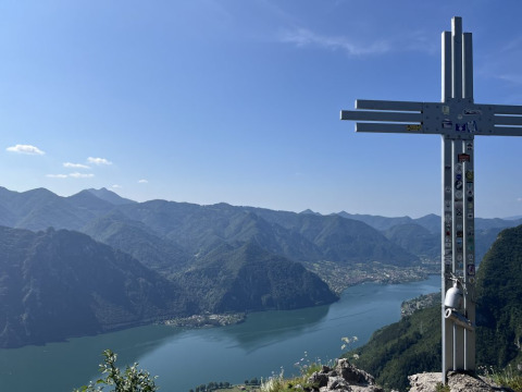 Vista panoramica dal campeggio Belvedere in Lombardia, Italia, con una croce sulla cima e lago sullo sfondo.
