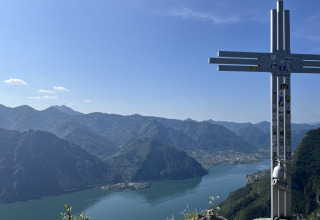 Vista panoramica dal campeggio Belvedere in Lombardia, Italia, con una croce sulla cima e lago sullo sfondo.
