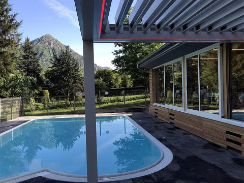Piscina all'aperto al Campeggio Belvedere, Lombardia, Italia, con vista monti e vegetazione rigogliosa.