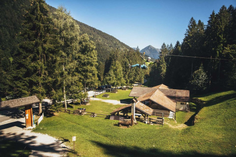 Vista del campeggio Belvedere in Lombardia, Italia, con zipline, case in legno e monti boscosi sullo sfondo.