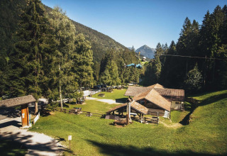Vista del campeggio Belvedere in Lombardia, Italia, con zipline, case in legno e monti boscosi sullo sfondo.