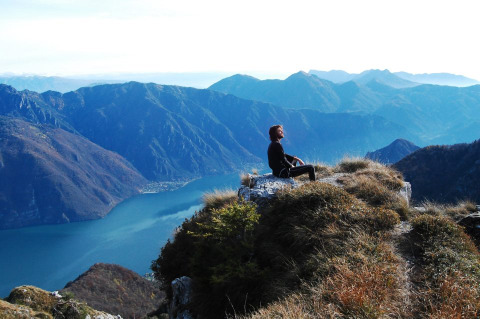 Una persona seduta su una roccia guarda il Lago d’Idro e le montagne vicino a Idro, Lombardia, Italia.