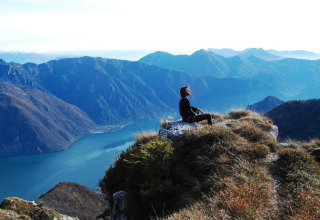 Una persona seduta su una roccia guarda il Lago d’Idro e le montagne vicino a Idro, Lombardia, Italia.