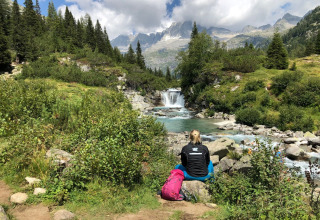 Persona seduta vicino al fiume con zaino al Campsite Belvedere, circondata da montagne in Lombardia.